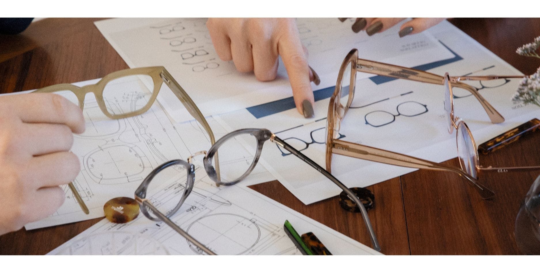 Reading glasses lying on a table with technical drawings and acetate samples